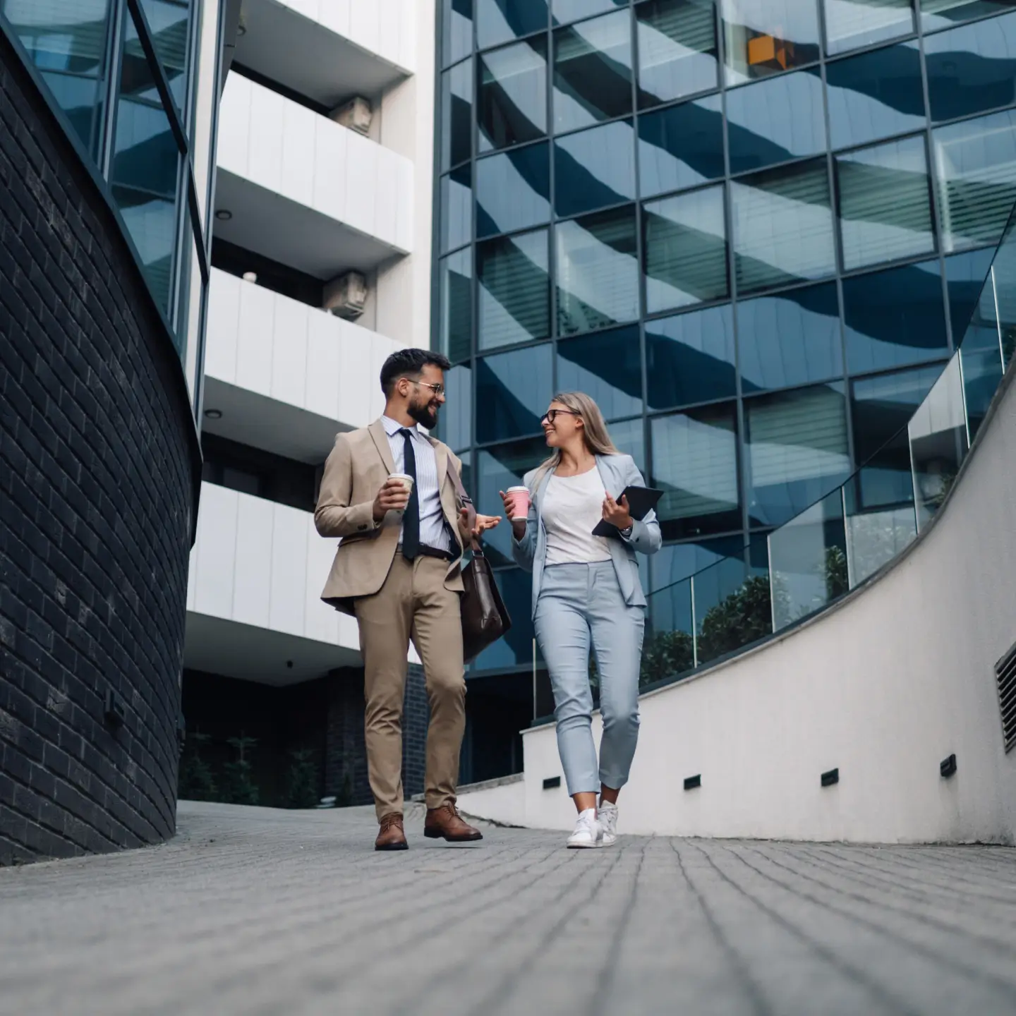 Two business professionals walking and talking outside a modern office building, holding coffee cups.
