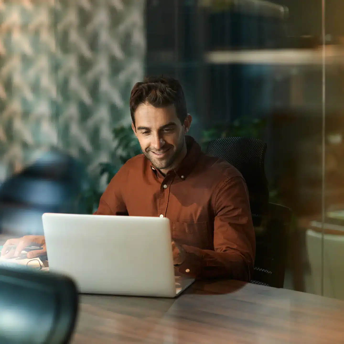 Man smiling while working on a laptop at a desk in a modern office.